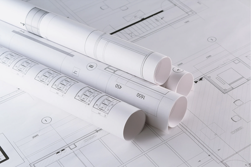 Rolled architectural blueprints on a desk, with a detailed floor plan in the background