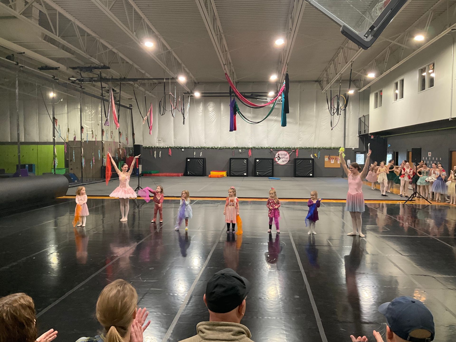 Children on a stage with a dance instructor. They are in costumes, with audience applause.