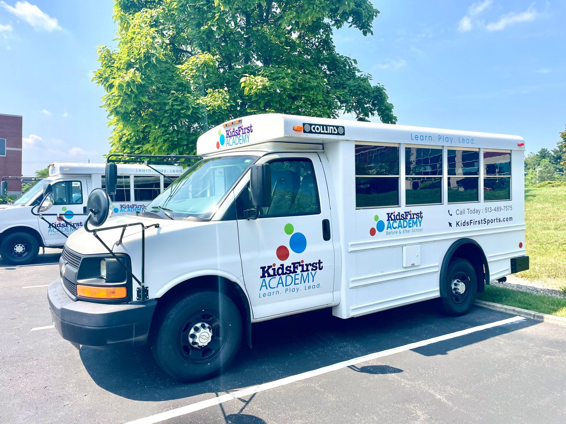 White KidsFirst Academy school bus parked in a lot. Another bus is partially visible behind it.