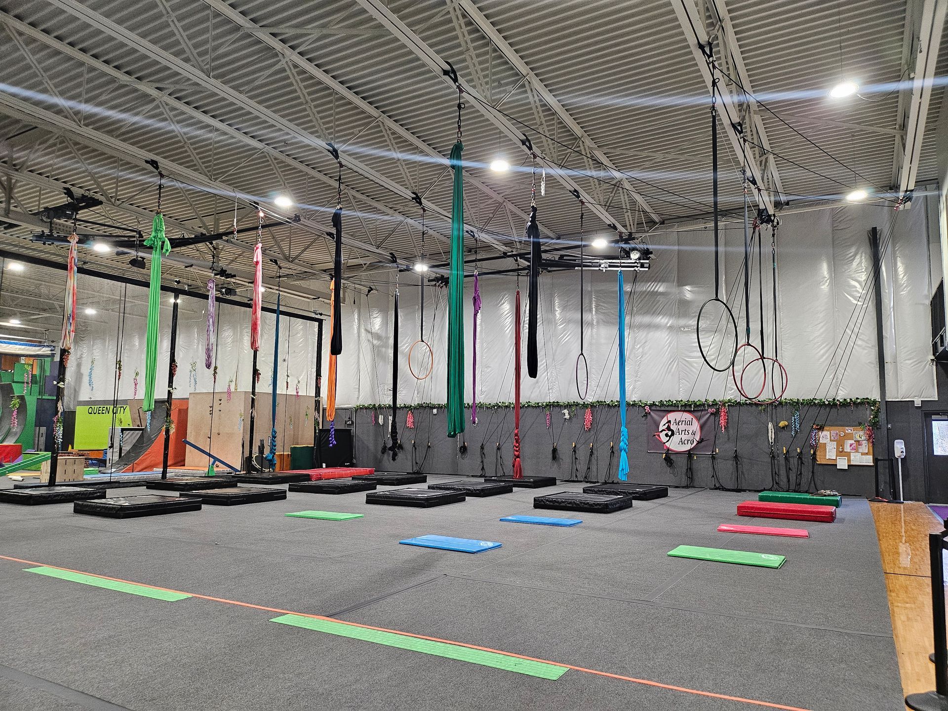 Gym interior with aerial silks, rings, and mats for various exercises.