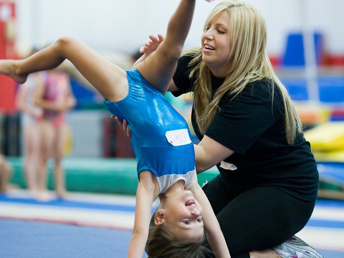 A woman is helping a young girl do a handstand on the floor