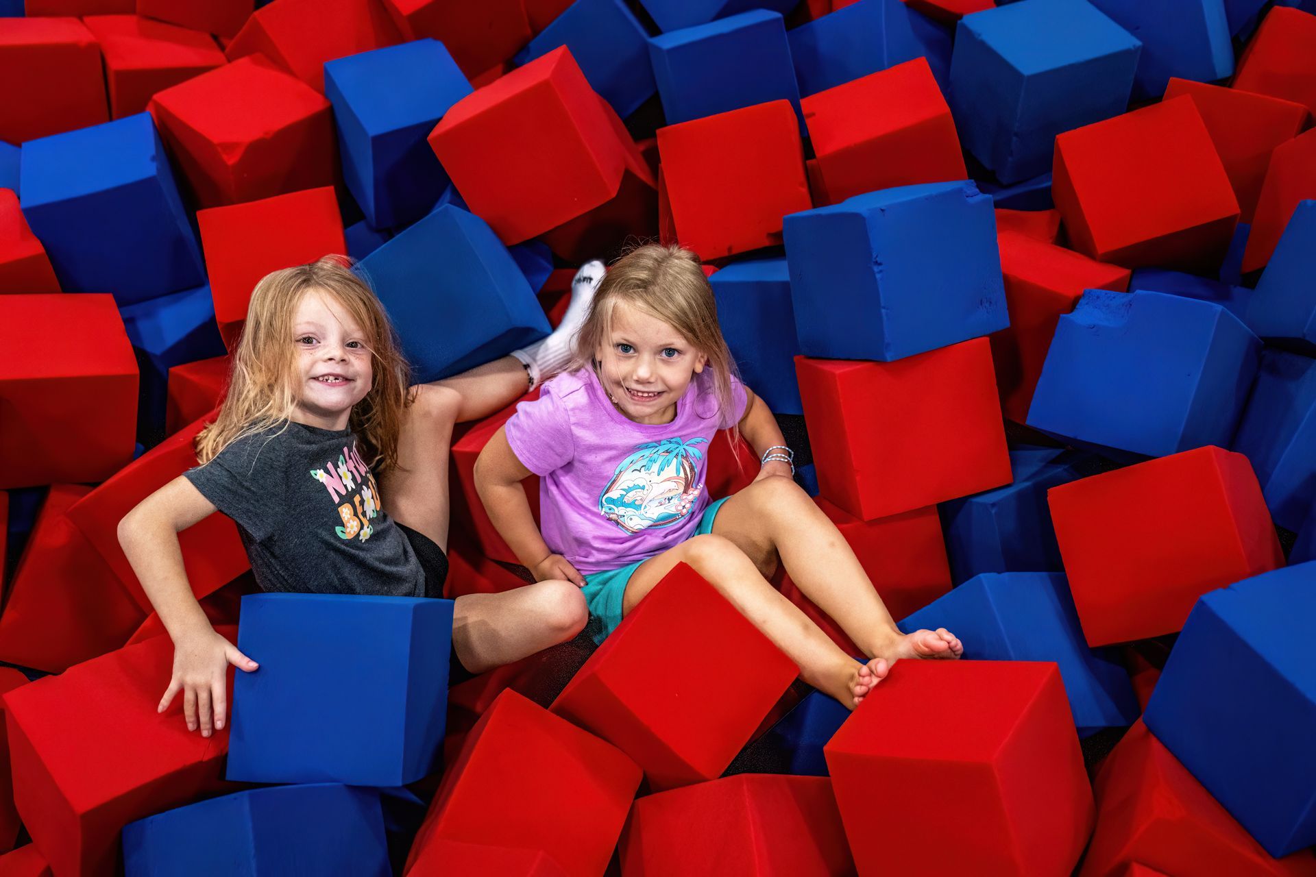 Two young girls sit among red and blue foam cubes, smiling at the camera.