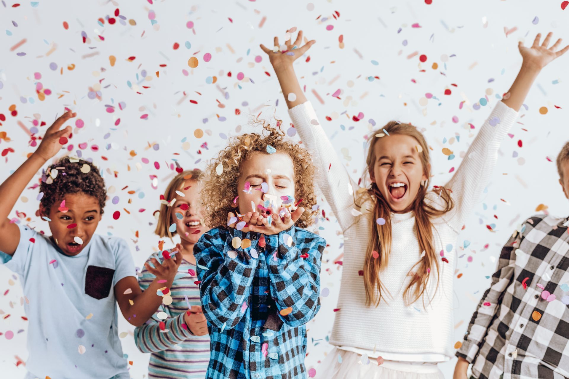 Children celebrating with confetti, arms raised, excited expressions, white background.