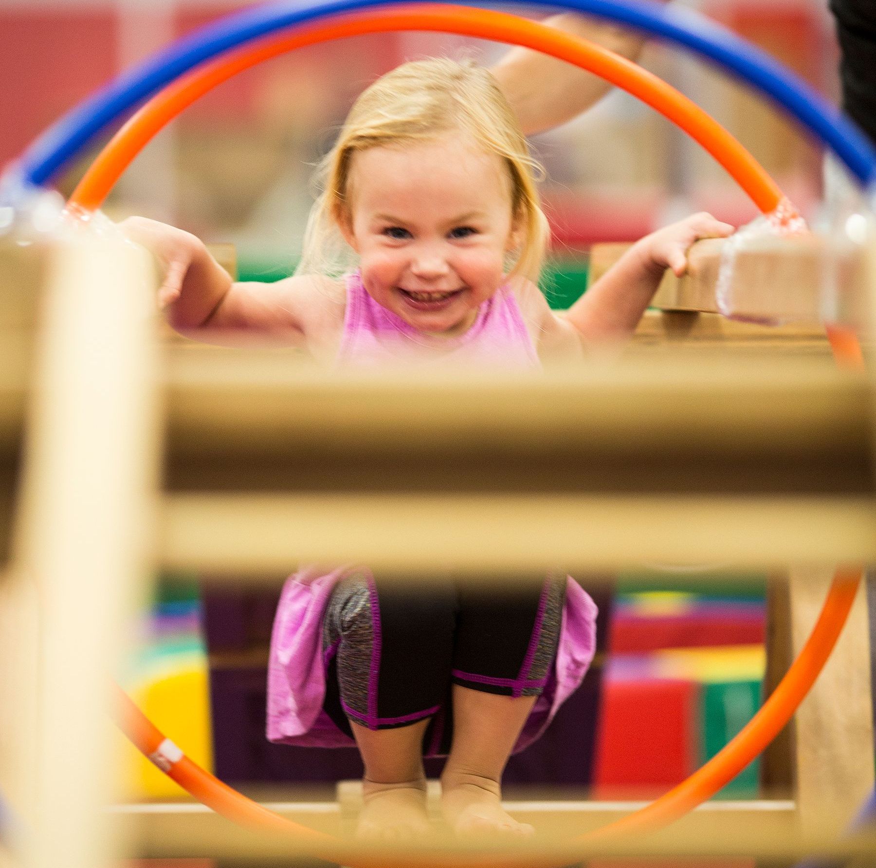 A little girl is sitting in a hula hoop and smiling.