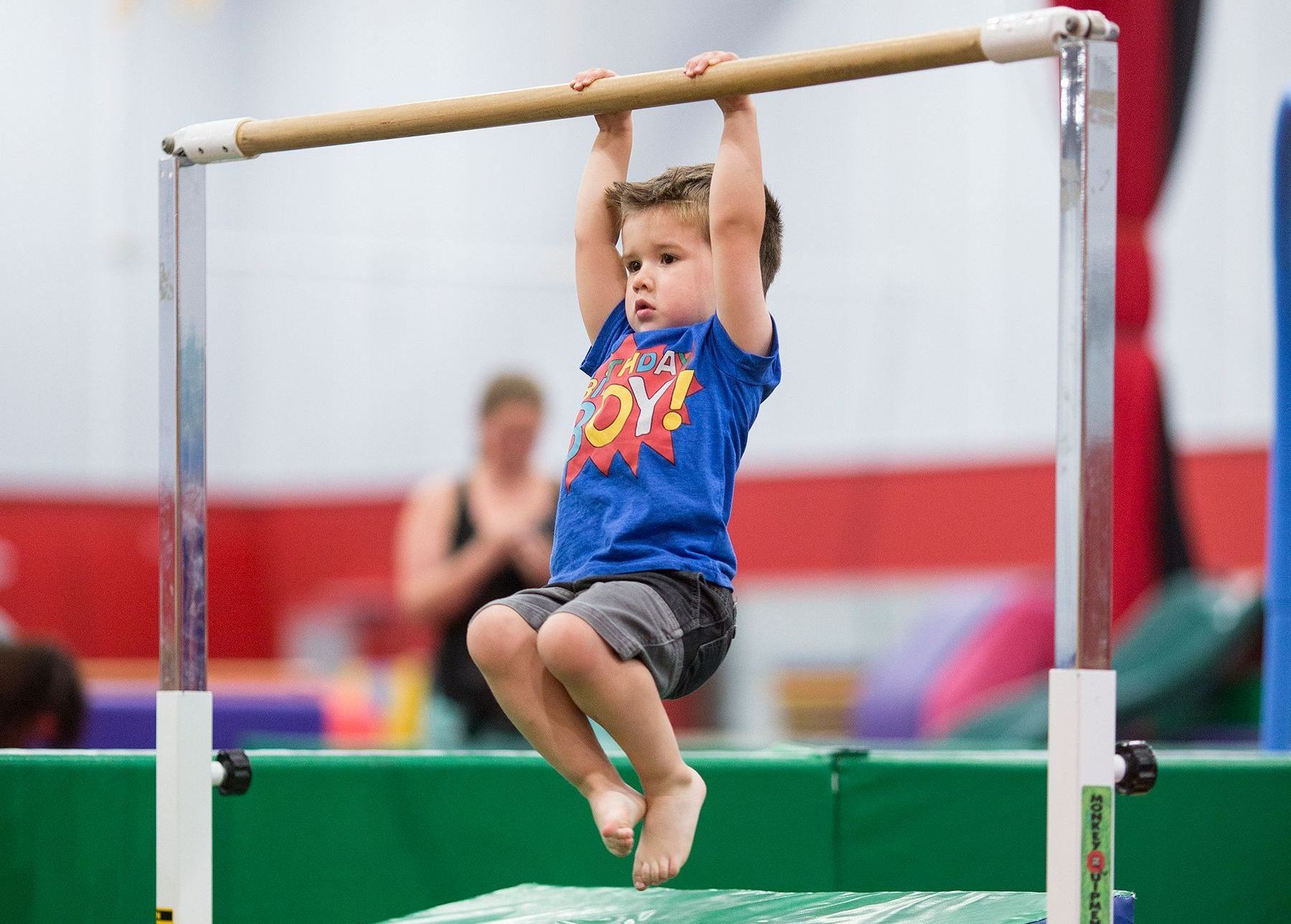 A young boy is hanging on a bar in a gym.