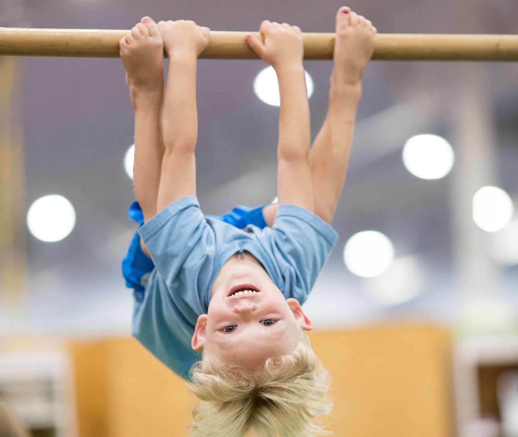 A young boy is hanging upside down on a balance beam.