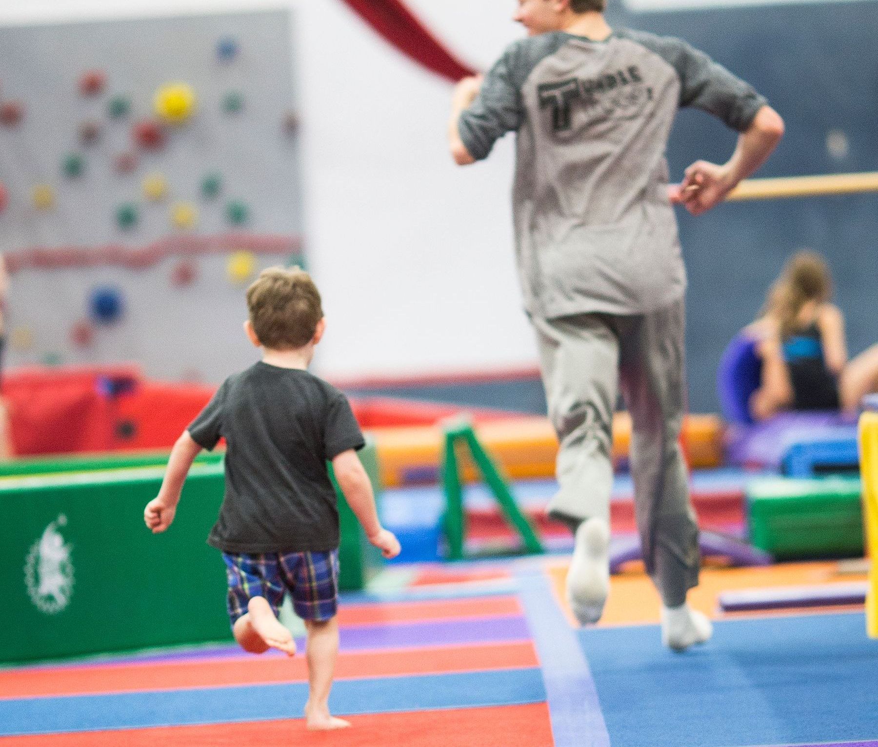 A man in a gray shirt with the word twinkle on the back is running with a little boy