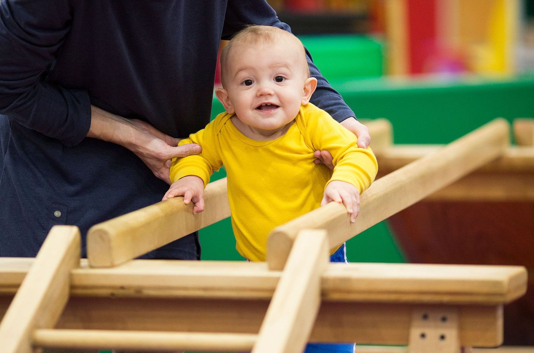 A baby is standing on a wooden balance beam.