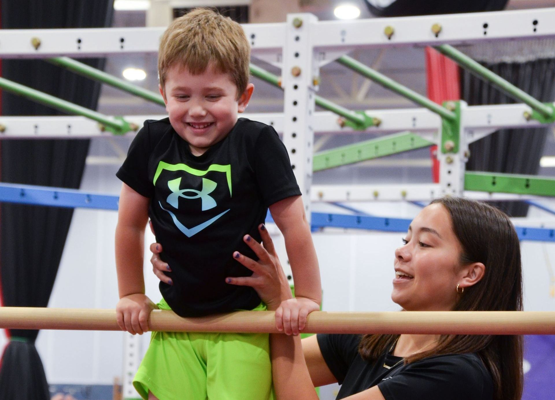 A woman is helping a young boy climb a balance beam.