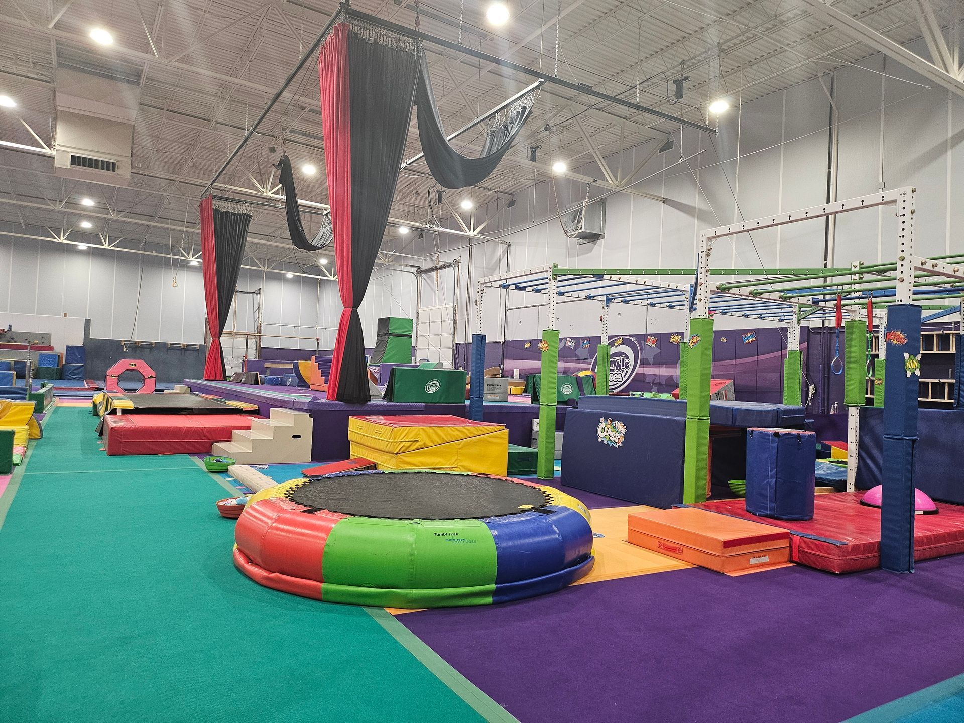 Indoor gymnastics gym with various colorful equipment and obstacles.