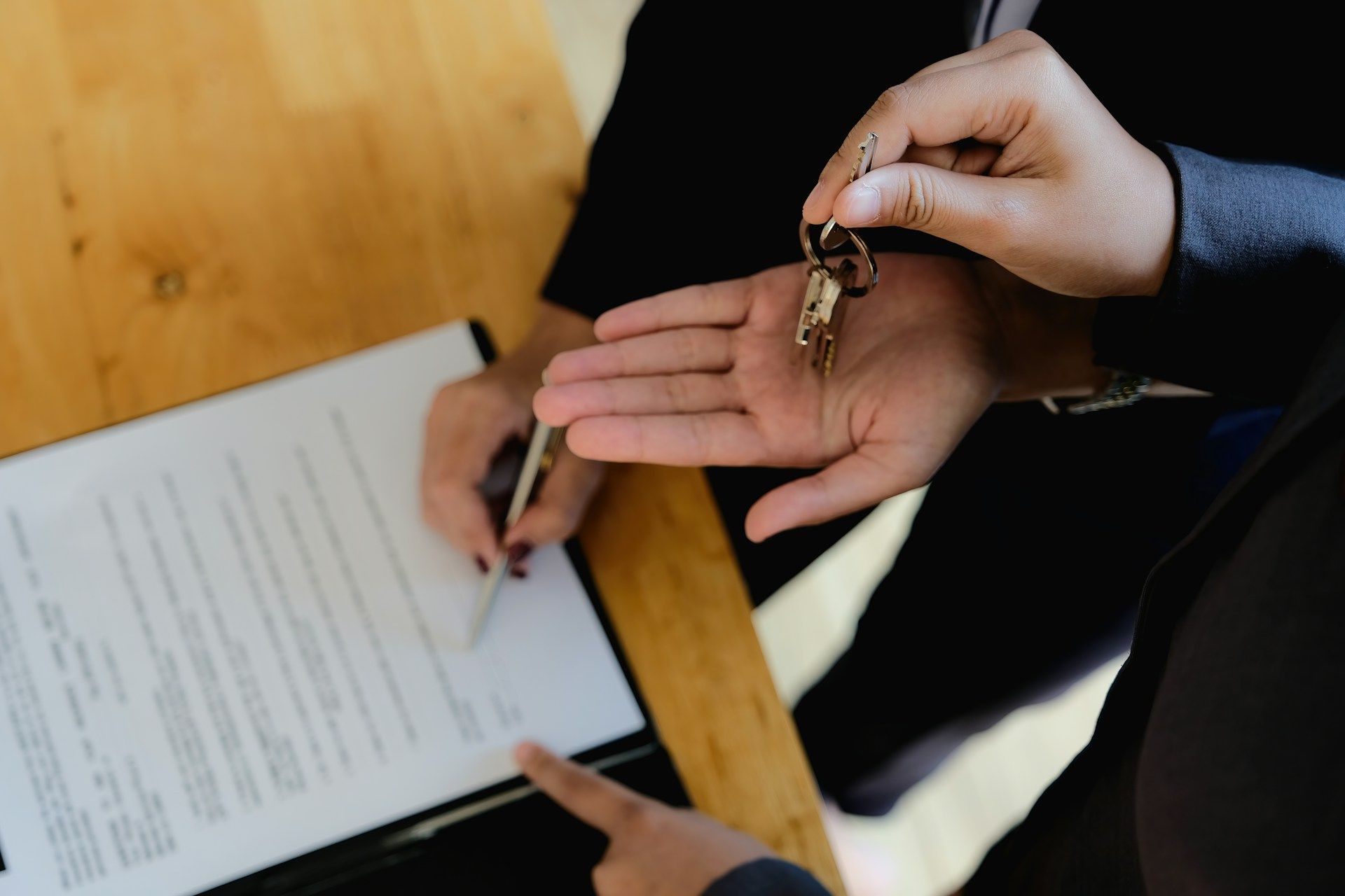 A person is holding a pair of keys in their hand while another person signs a document.