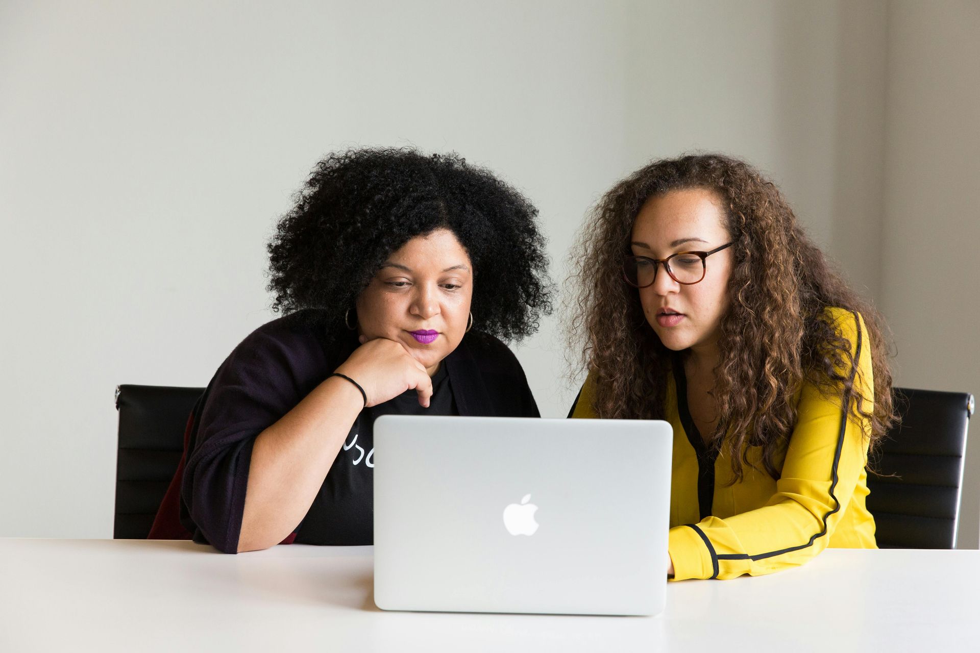 Two women are sitting at a table looking at a laptop computer.