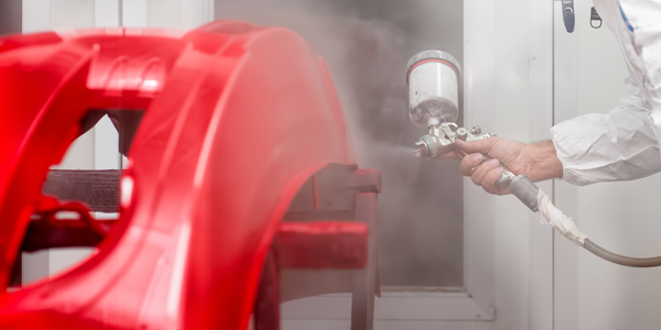 A person is spraying red paint on a red car.