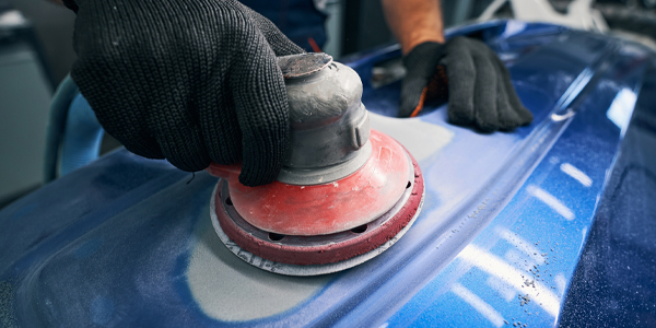 A person is sanding a blue car with a sander.