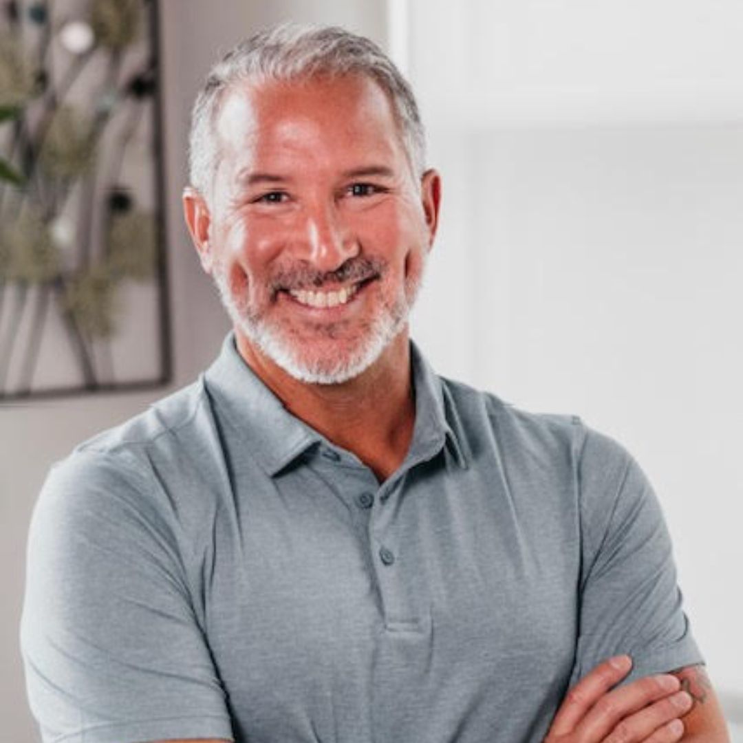 A man with a beard is smiling with his arms crossed.