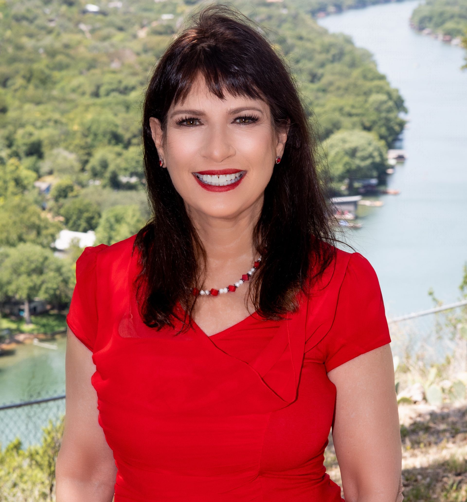 A woman in a red dress is smiling in front of a river.