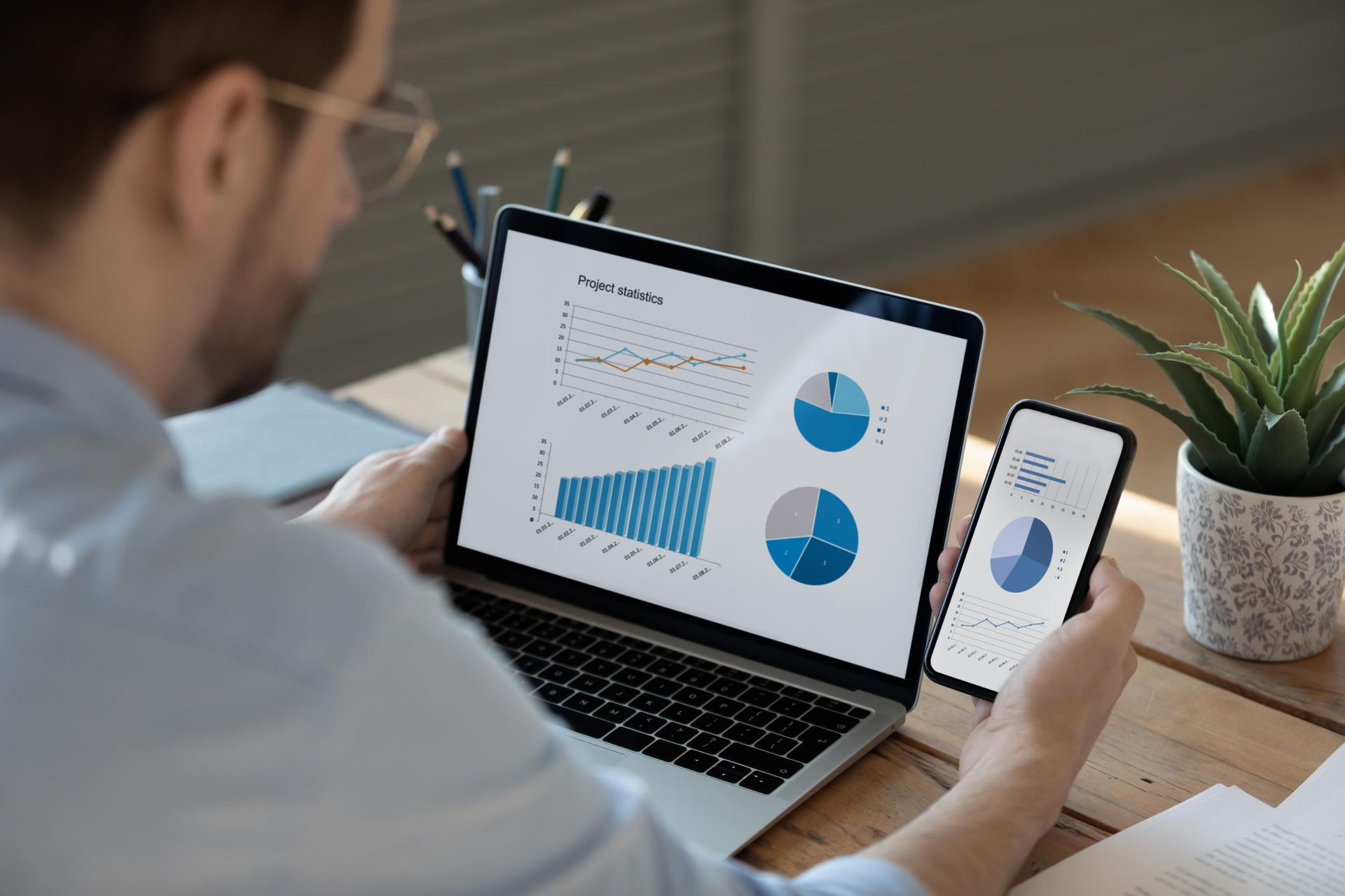 Man analyzing charts on a laptop and smartphone, likely business data. 
