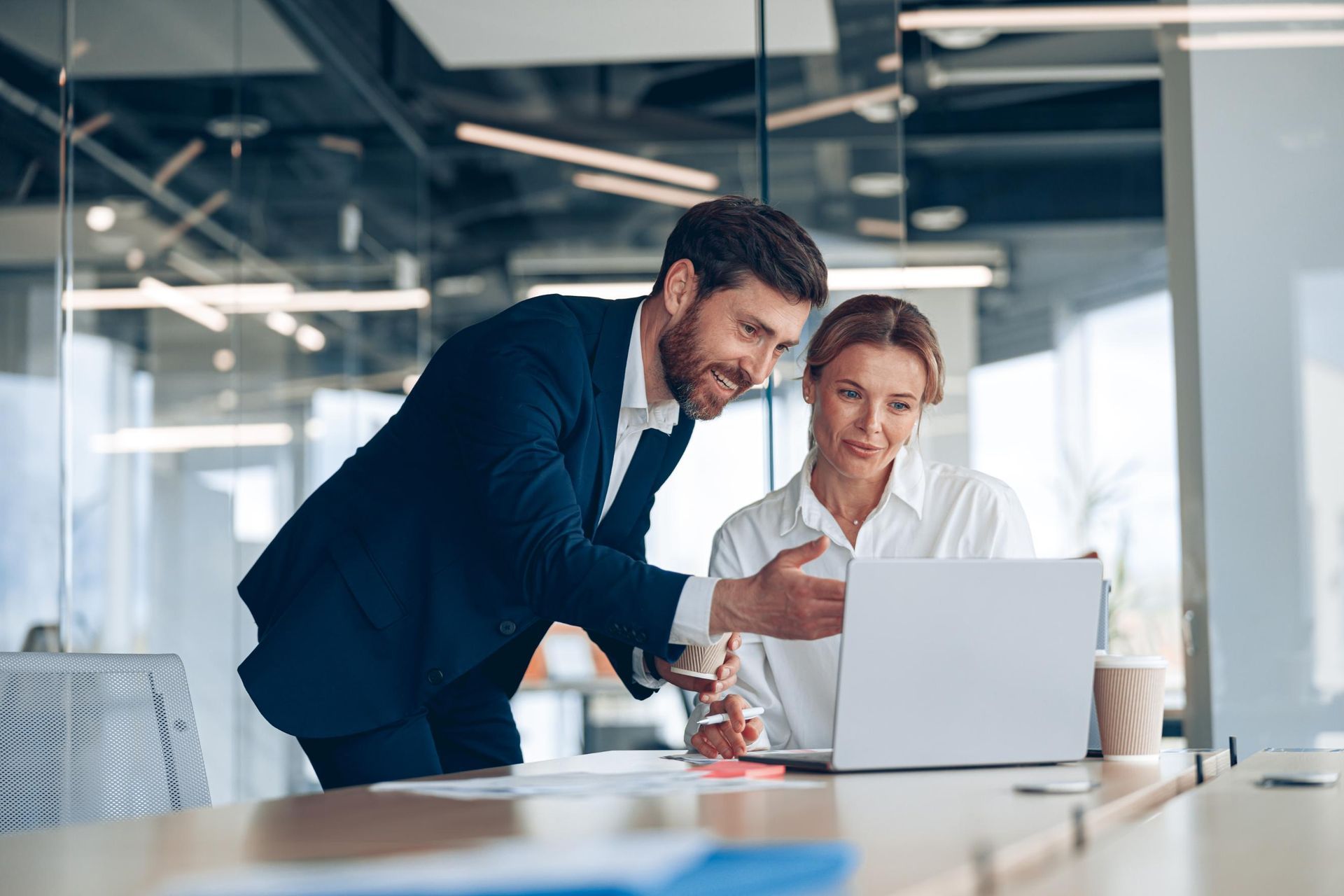 A man and woman in an office look at a laptop together. 
