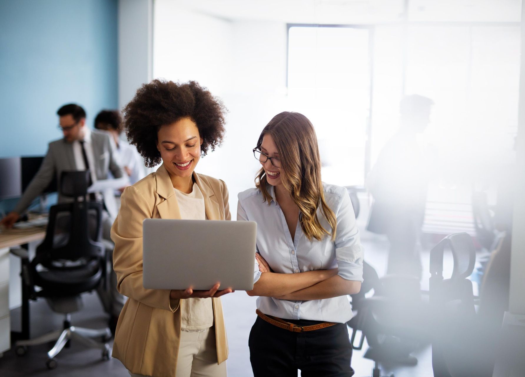 Two women in an office looking at a laptop, smiling. 