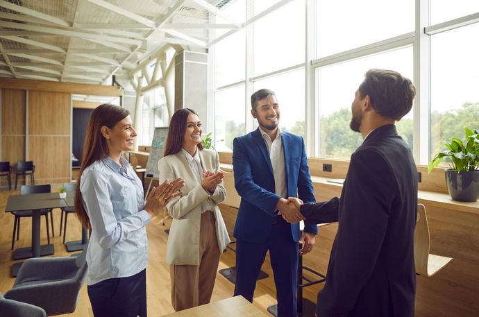 Group of business professionals shaking hands and celebrating in a modern office with a window.