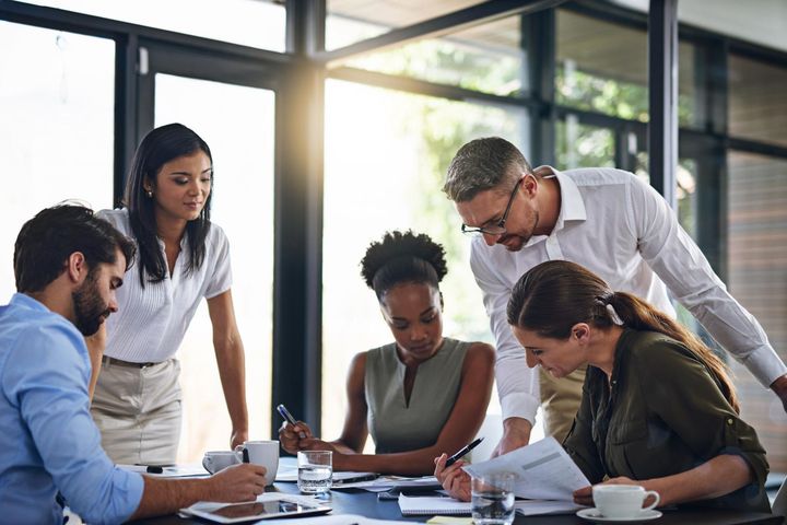 Team of diverse professionals collaborating around a table in a modern office, reviewing documents with focused expressions.