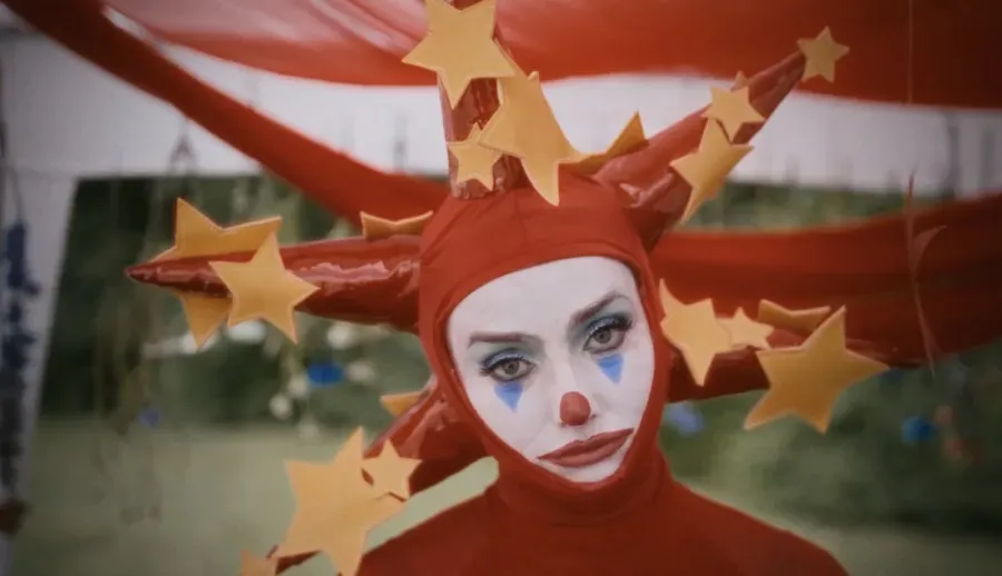 Person in red clown costume with star-shaped headdress, face makeup, looking at the camera.
