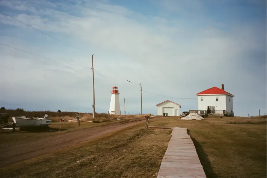 Shipwreck Point lighthouse with a red top, a small white building, and a larger white house with a red roof under a cloudy sky