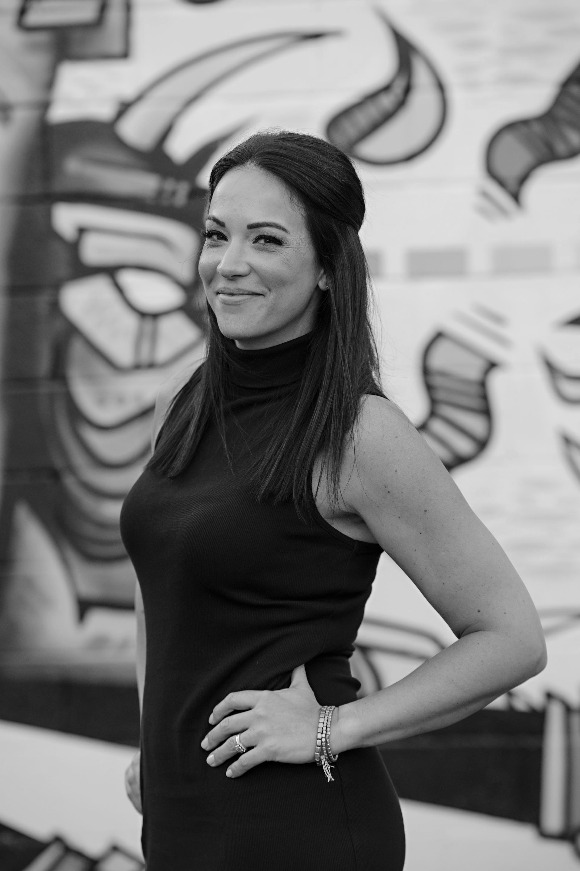 A woman in a black dress is standing in front of a graffiti wall.