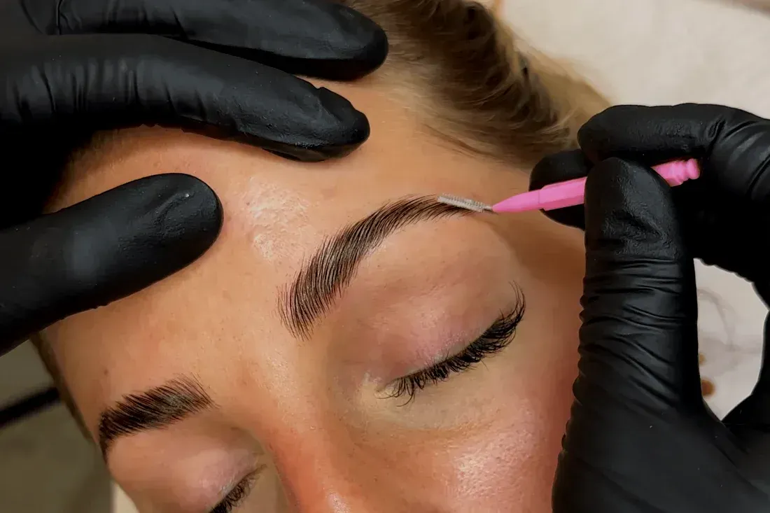A woman is getting her eyebrows done by a person wearing black gloves.