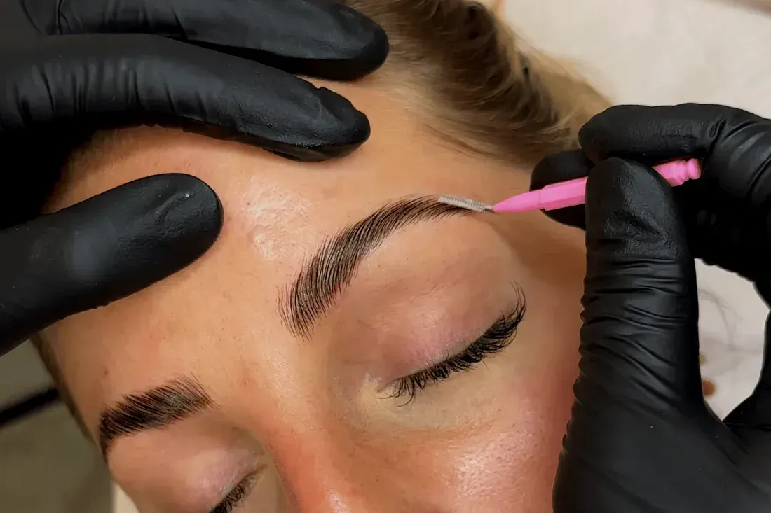 A woman is getting her eyebrows done by a person wearing black gloves.