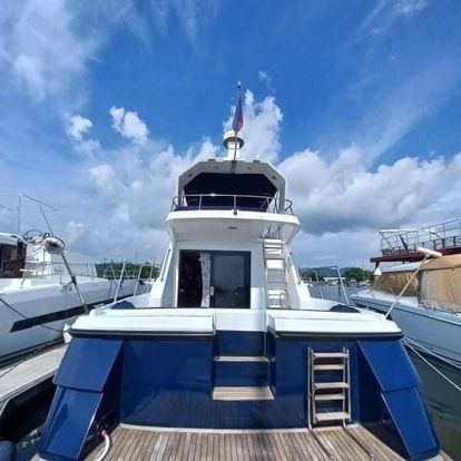 Rear view of a white and blue yacht docked under a blue sky with scattered clouds; a flag is on the top.