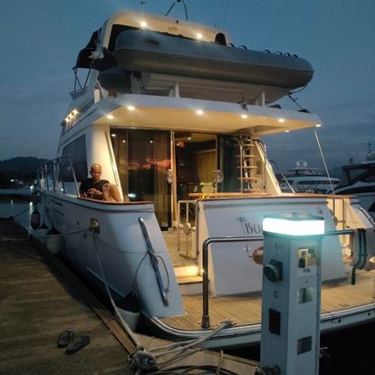 A person on a white yacht at dusk; the boat is docked at a marina and lit up.