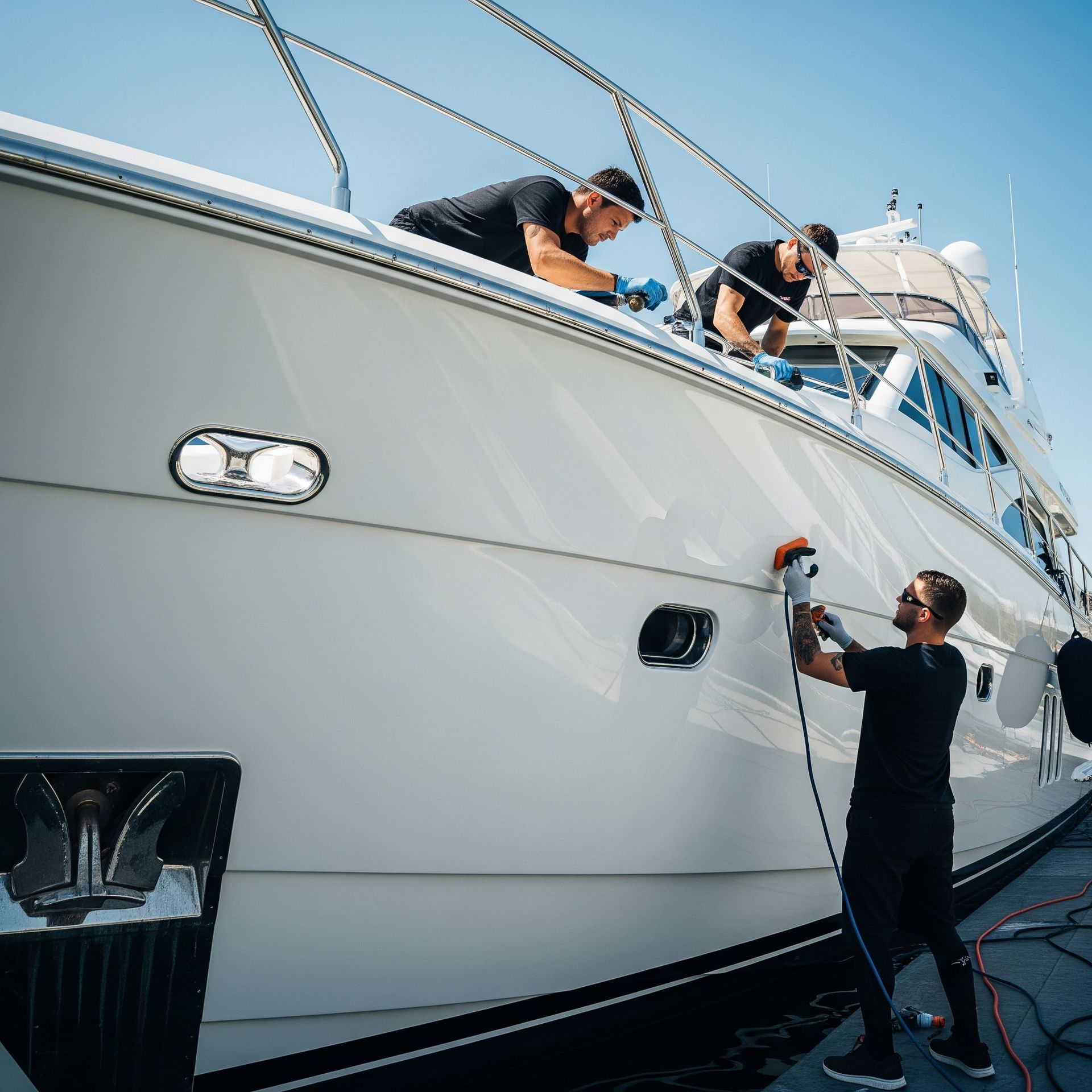 Two men are polishing the side of a white boat.