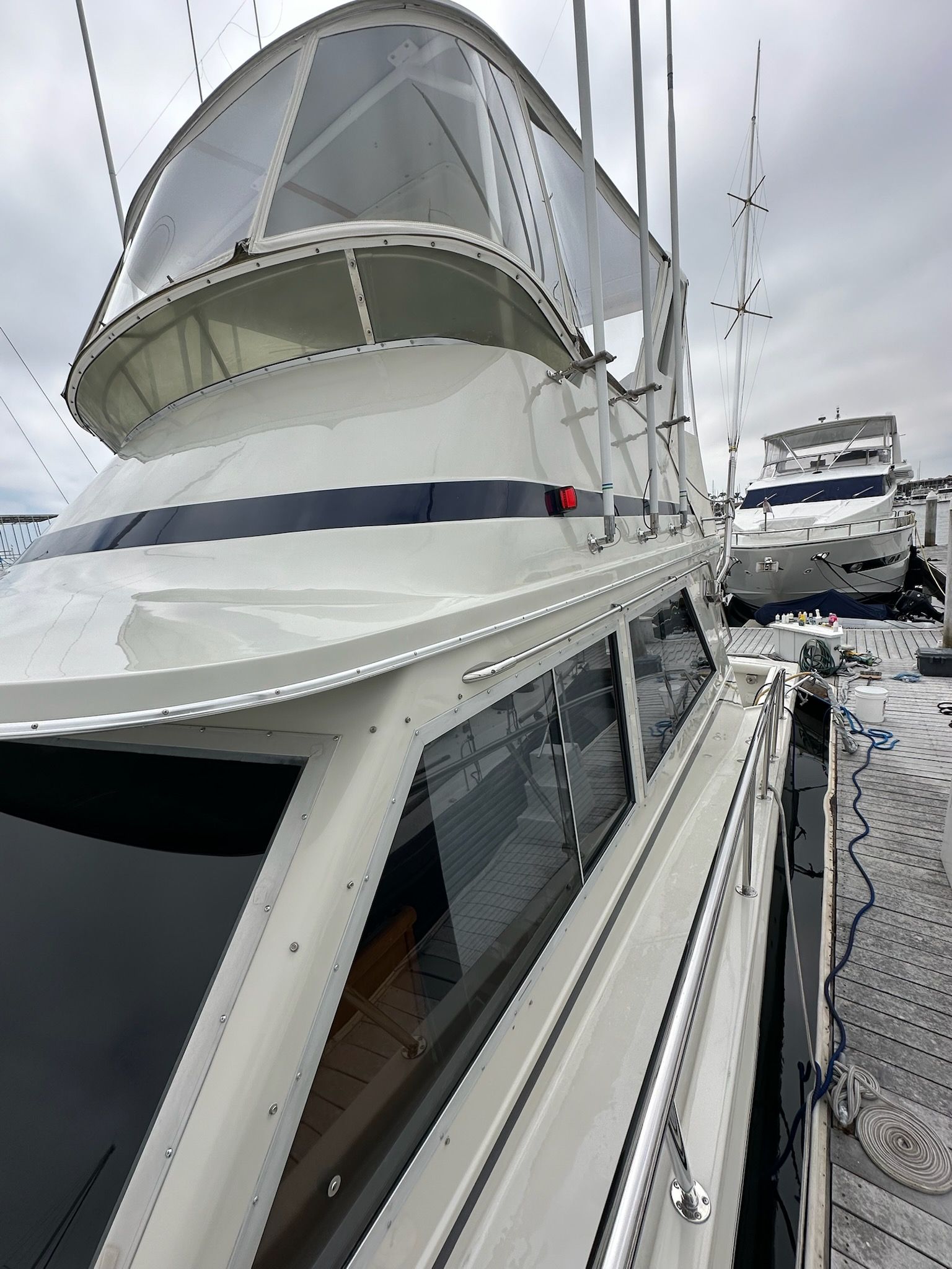 White yacht docked, with a clear view of the cabin and side windows, and a smaller boat behind it.
