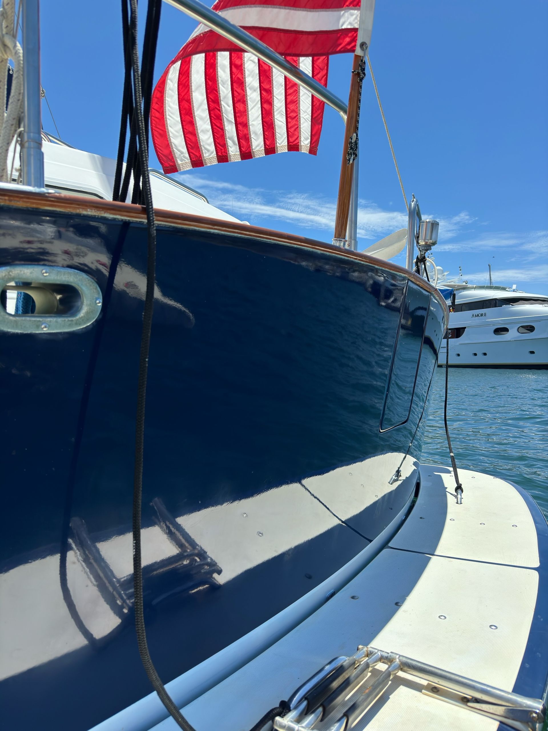 Blue sailboat hull with American flag flying, docked in a marina on a sunny day.