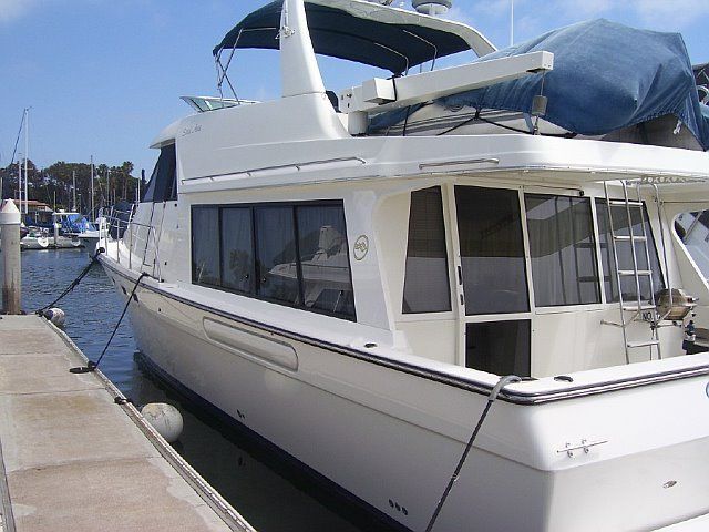 White motor yacht docked at a marina, with blue tarp covering part of the deck.