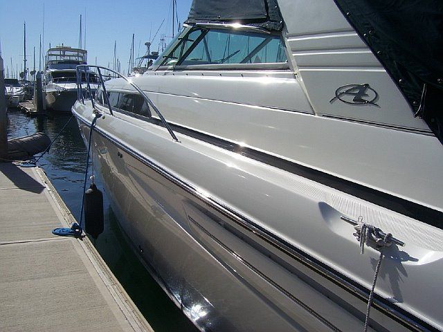 White motorboat docked at a marina on a sunny day. The boat is next to a concrete pier.