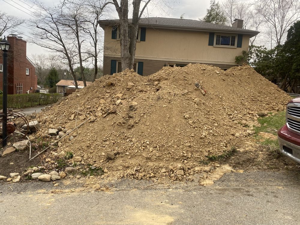 Large pile of dirt in front of a two-story beige house. A red truck is parked to the right. Overcast sky.