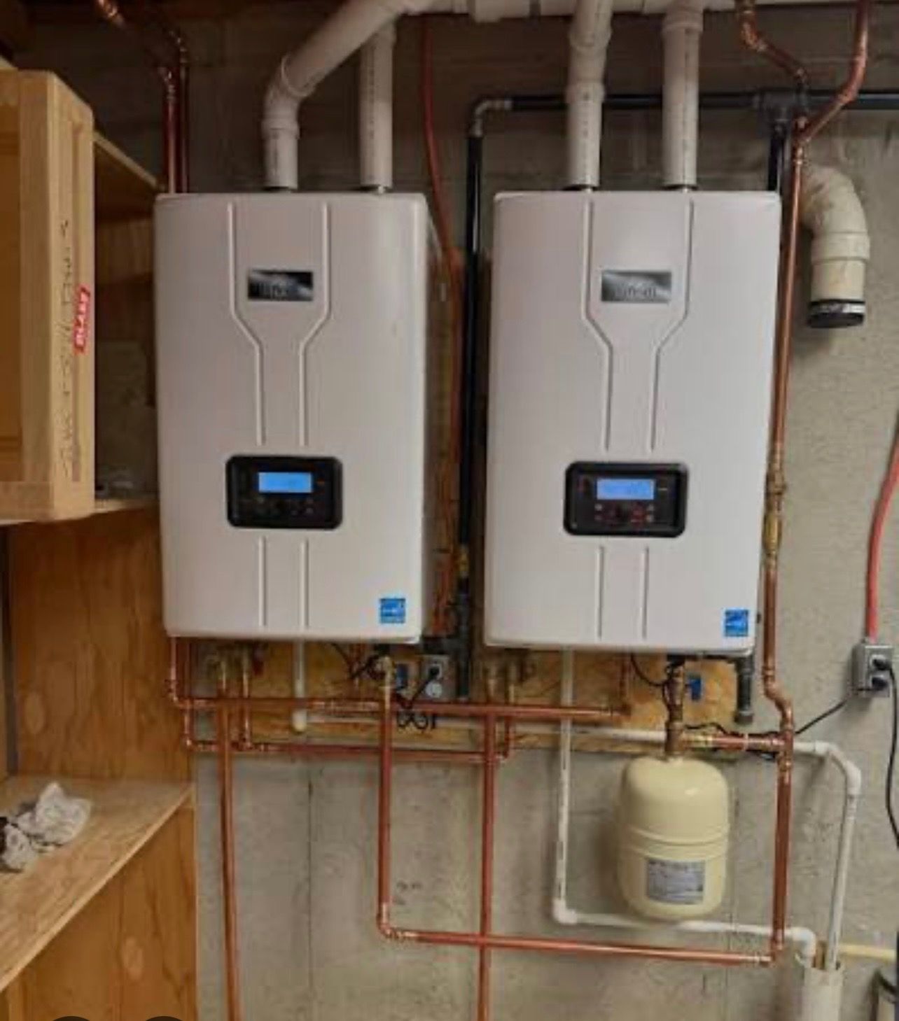 Two white wall-mounted tankless water heaters with copper pipes in a utility room.