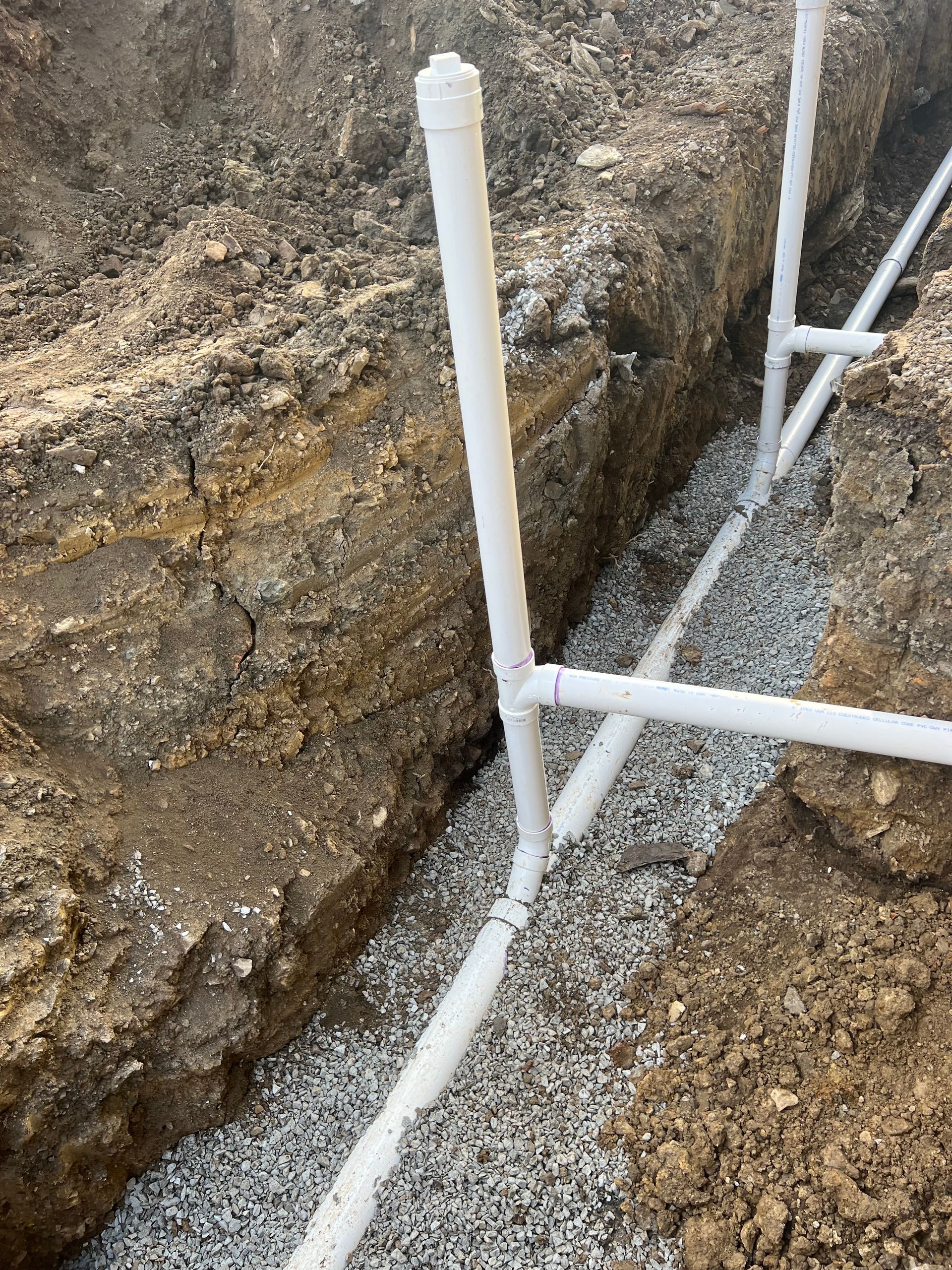 White PVC pipes in a trench filled with gravel, likely for irrigation.