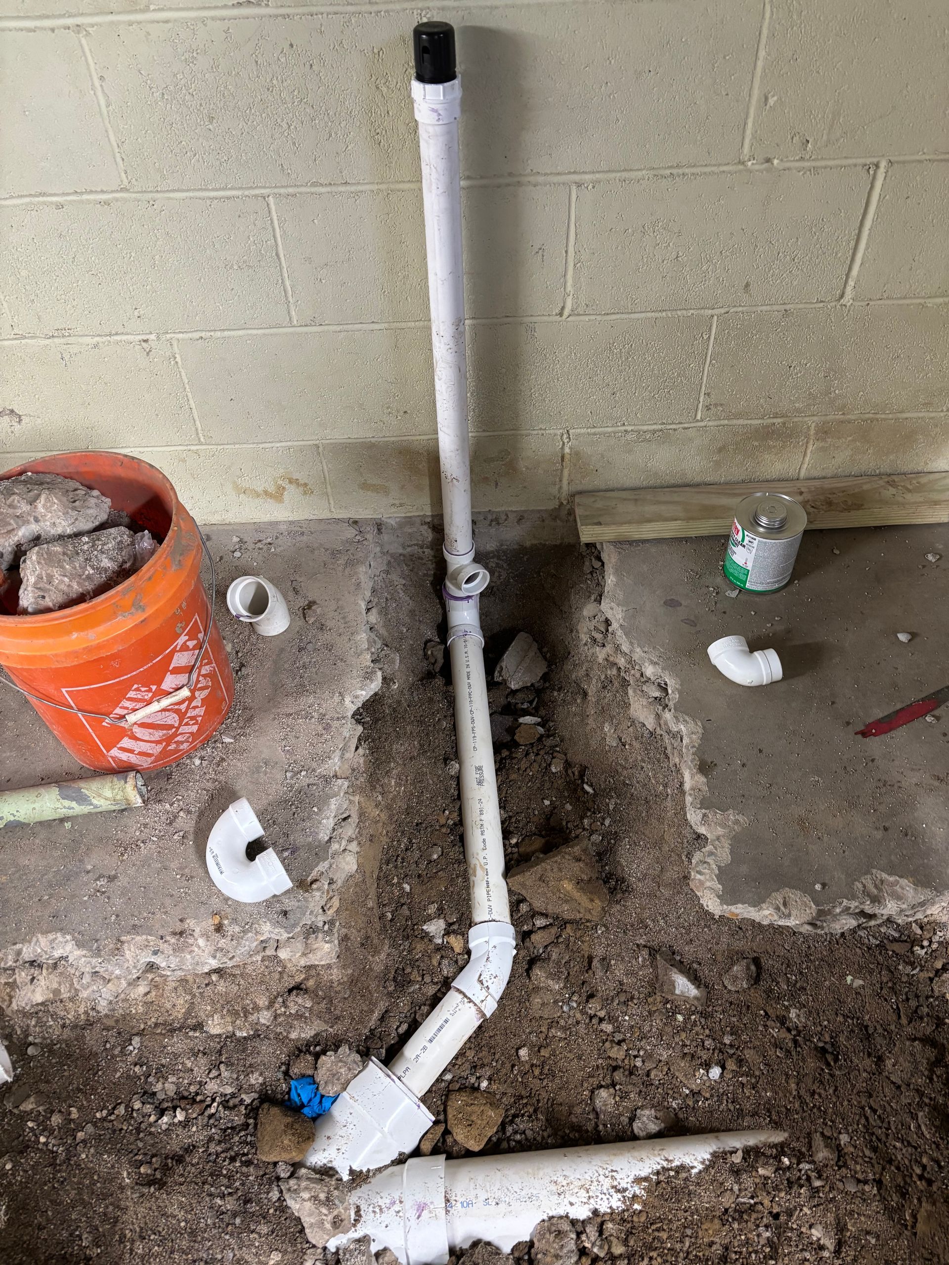 White PVC plumbing pipes installed in a basement floor trench.
