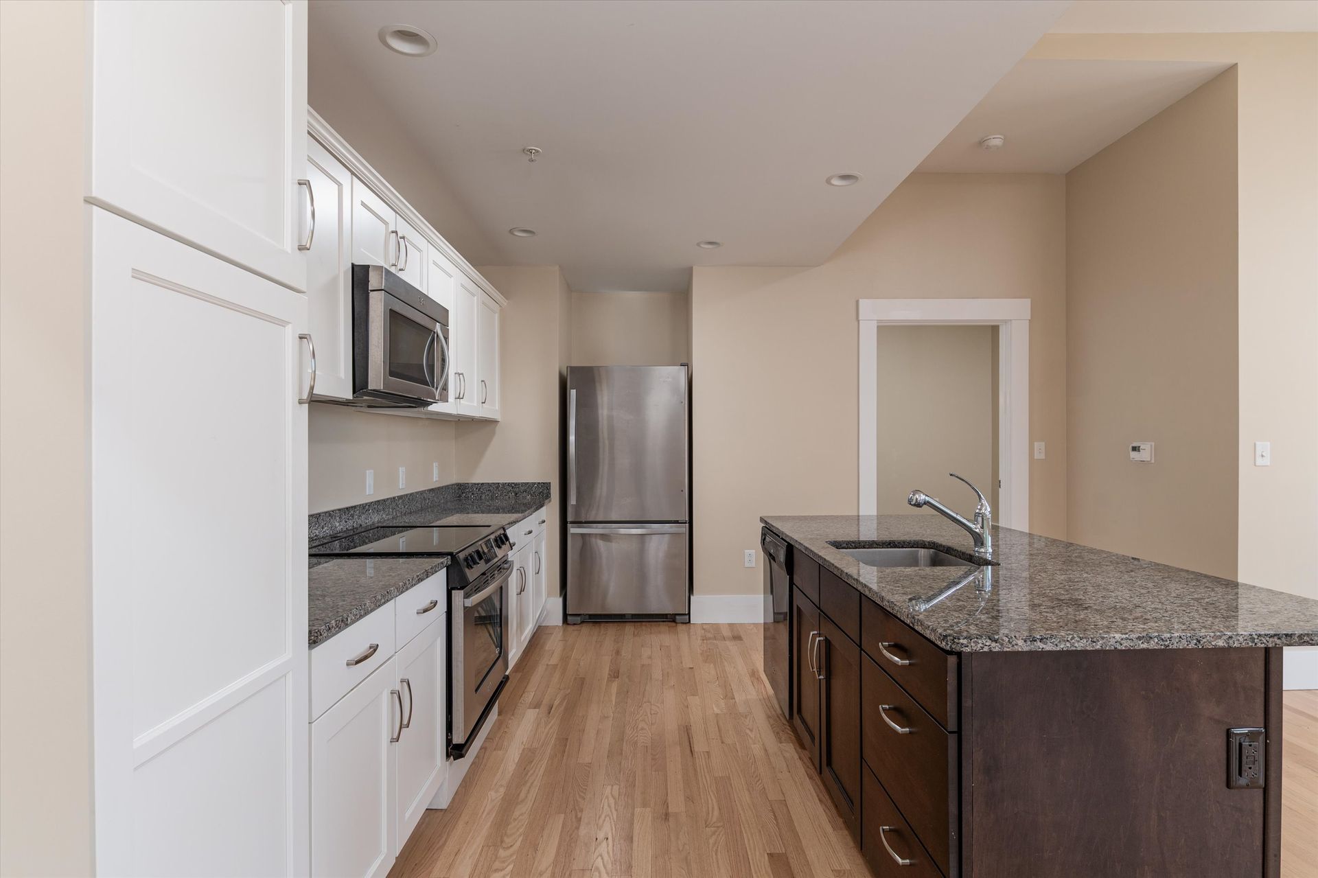 A modern kitchen with white cabinets, dark island base, granite countertops, and stainless steel appliances.