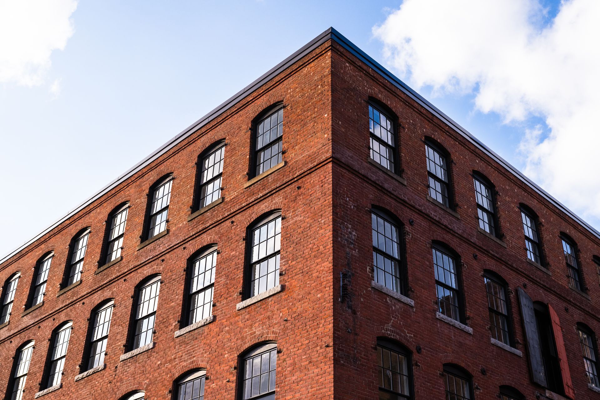 Red brick corner building with rows of black-trimmed windows against a blue sky