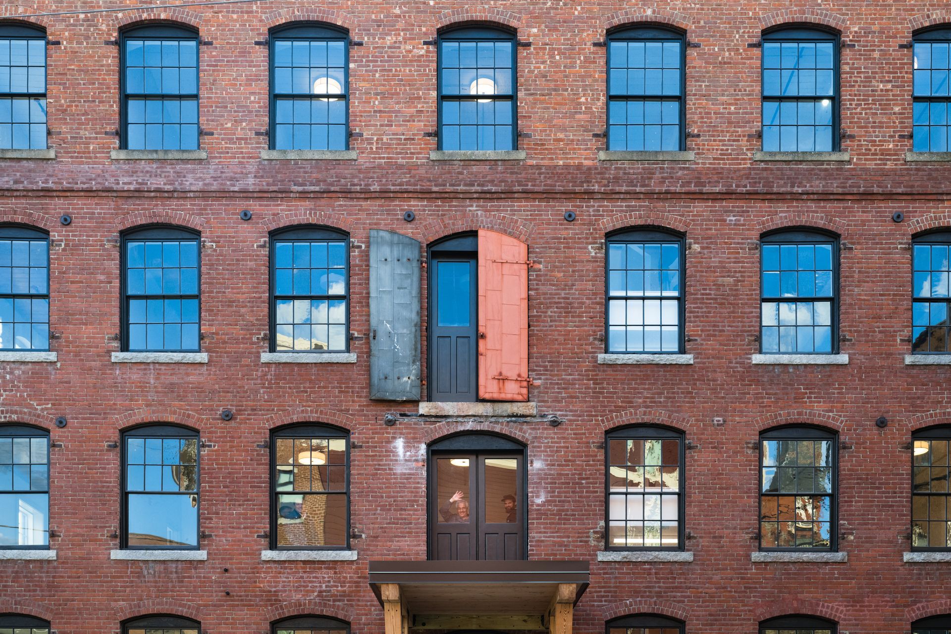 Brick apartment building facade with blue windows and one open orange window shutter