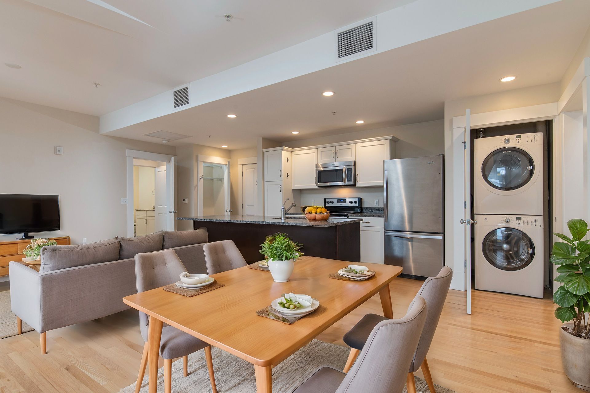 A modern, open-concept apartment featuring a dining area, living space, stainless steel kitchen, and a stacked washer-dryer.