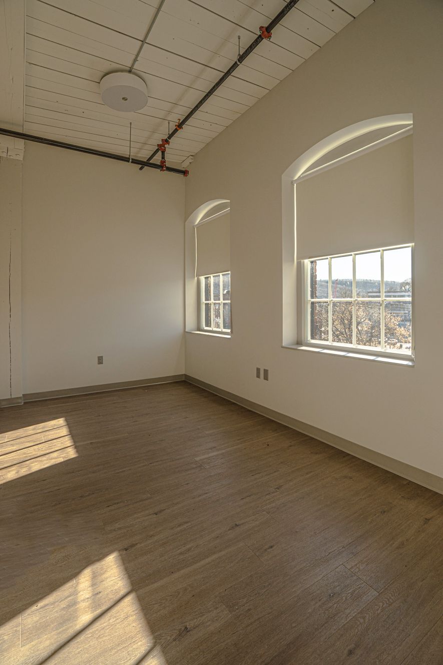Empty sunlit room with wood floors, white walls, and two arched windows casting shadows.