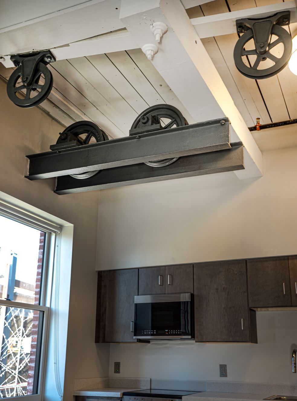 Kitchen with a decorative hanging wagon-wheel cart above cabinets and a window.