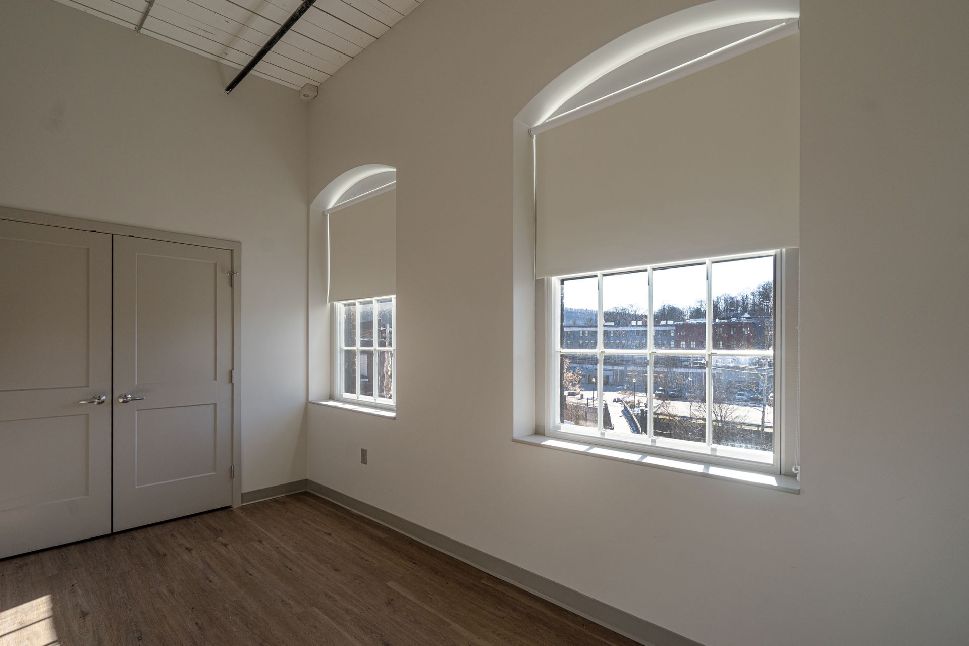 Empty room with white walls, arched windows, and wood flooring, lit by daylight