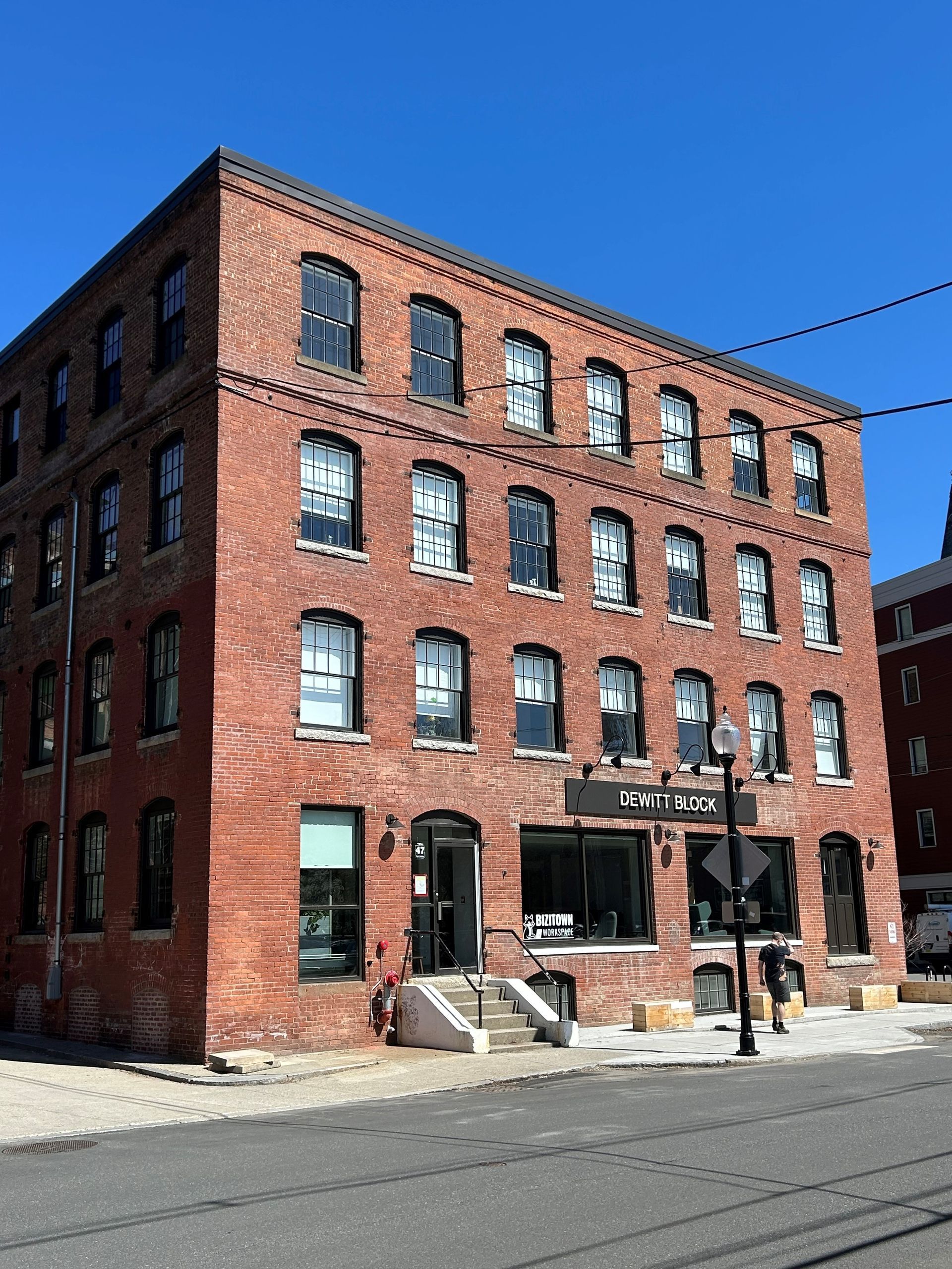 Red brick industrial building with black awning and rows of windows on a sunny street corner