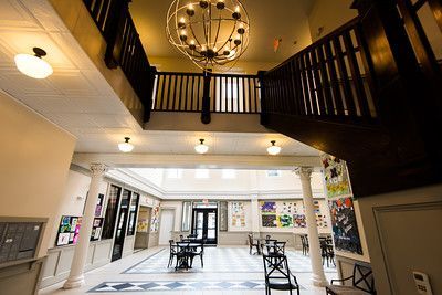 Interior of a multi-story building atrium with a large globe chandelier, wooden staircase, and seating area.